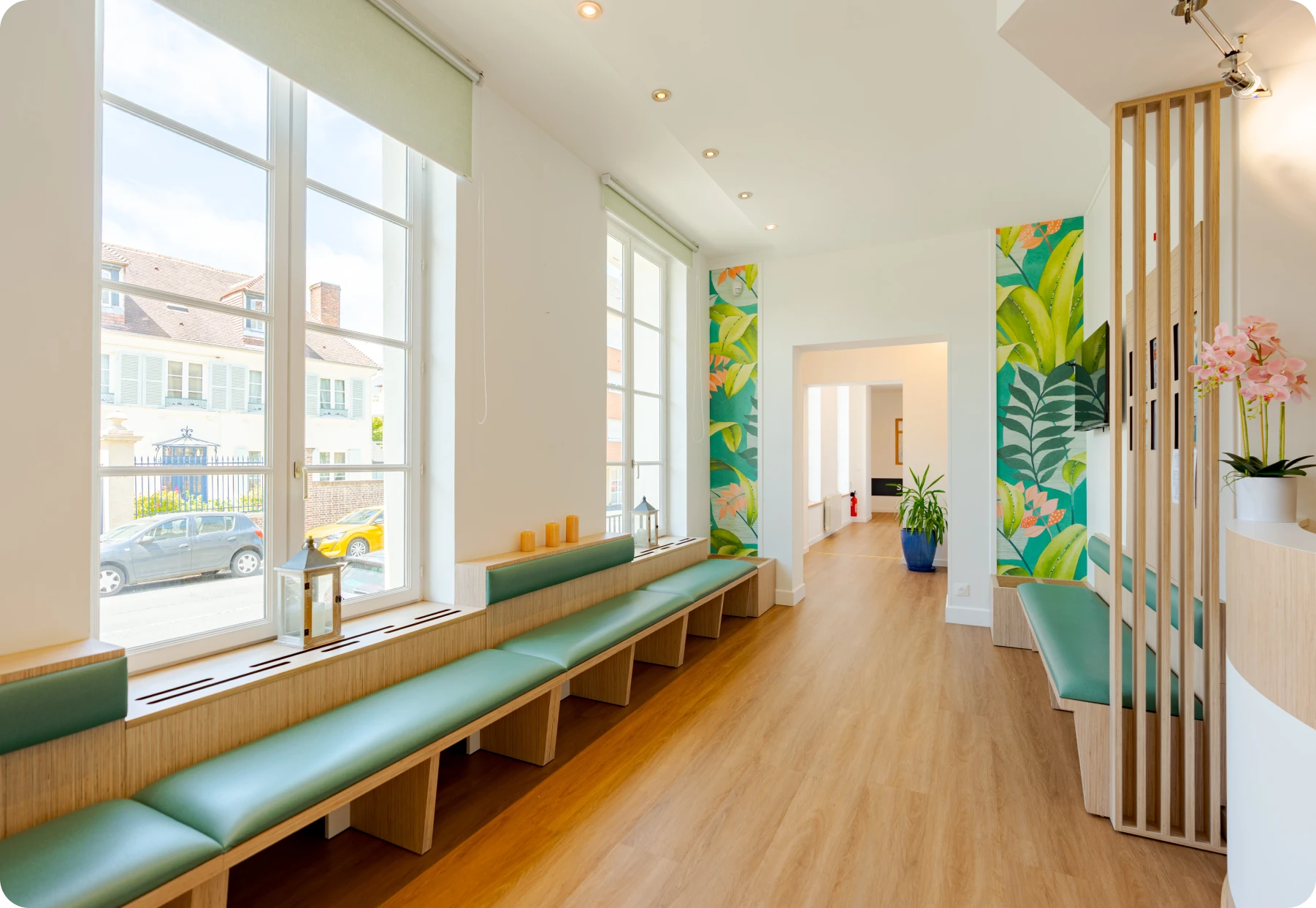 Couloir lumineux du cabinet d'orthodontie avec banquette verte et grandes fenêtres sur rue